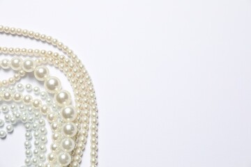 Beautiful pearl necklaces on white background, flat lay. Space for text