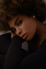 a close-up portrait of a person with curly hair, wearing a black top and an earring