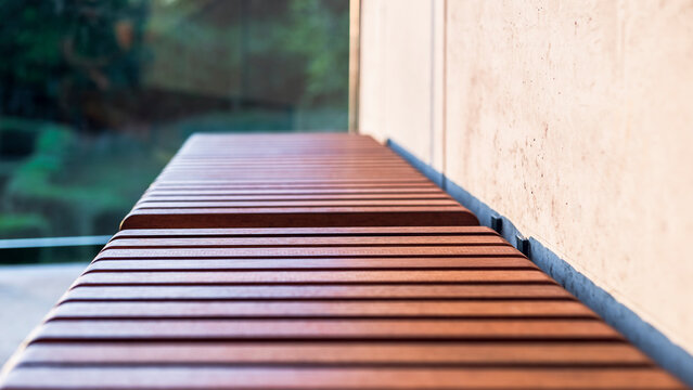 Wooden slats on the bench seat. Exotic Iroko wood. Detail. Close up. Architectural concrete wall and greenery in the background