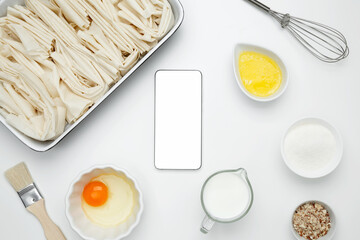 Cooking ingredients and smartphone with blank screen on a white background. For baking Crinkle Cake. Mockup design for recipe or food blog