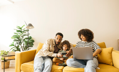 Family members relaxing on a bright yellow sofa and playing video games while the mother is using a...