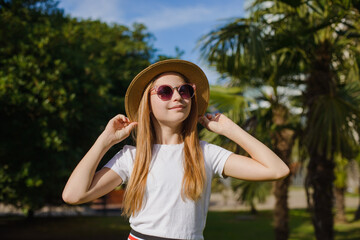 A teenage girl with long hair against the sky in a park wearing a hat and sunglasses