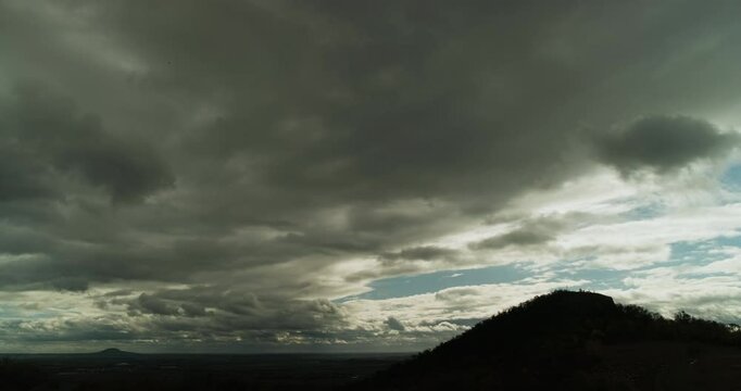 Low Gray Cloud Blanket Drifts Fast Over a Wooded Hill Silhouette Revealing Only Occasional Patches of Blue Sky in a Wide Rural Time Lapse of Moody Weather Light and Quiet Landscape Rhythm