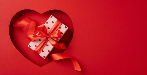 Red heart cutout with a gift box and ribbon creates a romantic Valentine's Day theme on bright...