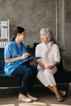 Asian caregiver doctor examine older patient woman therapist nurse at nursing home taking care of senior elderly woman sit on sofa