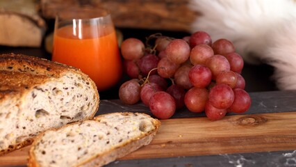 Sliced seeded bread, juicy grapes, vibrant orange juice arranged on wooden surface create warm, inviting scene for seasonal harvest brunch, ideal for fall-themed gatherings, organic food promotions.