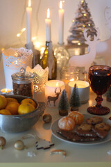 Various Christmas decorations, cookies, chocolate, nuts and tangerines, wine glasses and lit candles on the table. Holiday hygge at home. Selective focus.