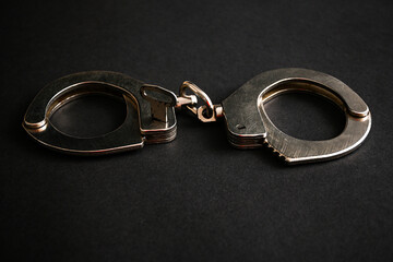 Steel handcuffs lying on a dark background, representing concepts of crime, arrest, law enforcement, and security