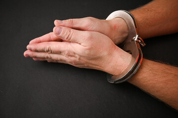 Handcuffed man showing his wrists on a dark background