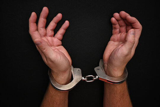 Handcuffed man showing his wrists on a dark background
