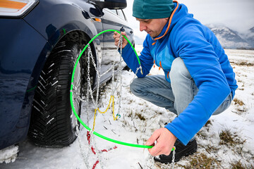 Man installing snow chains on car tire during winter, ensuring safety on snowy roads