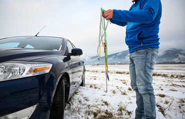 Man installing snow chains on car tire during winter, ensuring safety on snowy roads