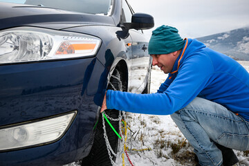 Man installing snow chains on car tire during winter, ensuring safety on snowy roads