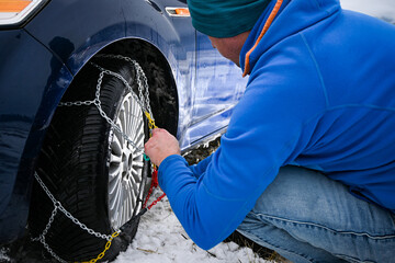 Man installing snow chains on car tire during winter, ensuring safety on snowy roads
