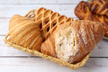 Different pastries in basket on white wooden table, closeup