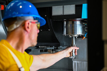 Metalworker is changing the drill bit in a cnc machine during a metal processing operation