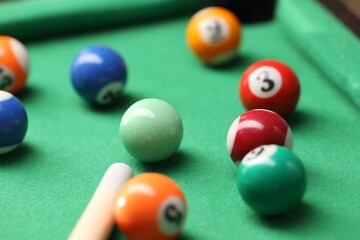 Many colorful billiard balls and cue on green table, closeup