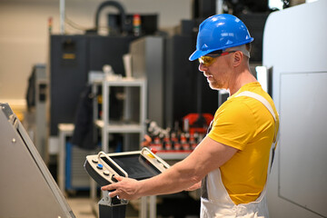 Factory worker wearing safety glasses and hardhat operating industrial machinery using control...