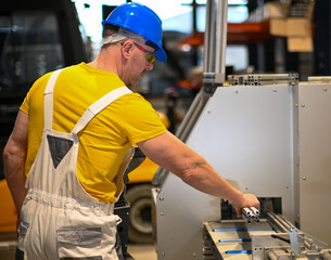 Factory worker operating machinery and holding a metal part, wearing safety gear, demonstrating...