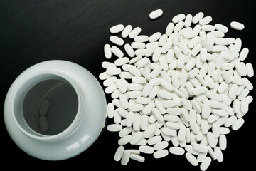 White tablets spilled from a container on dark surface