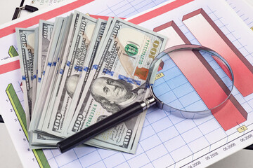 Close up of dollar banknotes and magnifying glass on chart background