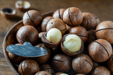 Macadamia nuts with a metal key for opening the shell in wooden bowl, closeup