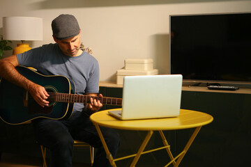 A man sitting in front of the computer practicing online music lessons