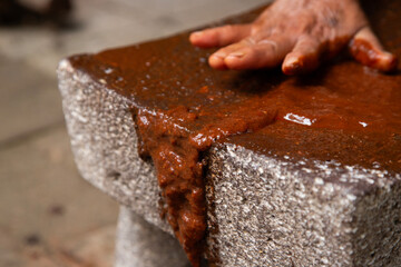 Woman from an indigenous community in Oaxaca preparing traditional Mole Rojo with a metate, a tool for grinding ingredients in Mexico.