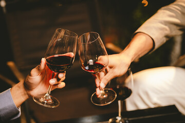 Close-up photo of people congratulating, toasting and touching wine and champagne glasses at a garden party with friends on a warm summer day.