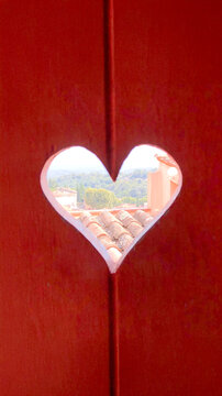 Red shutter with a heart cut out, showing the French Provence countryside through the heart