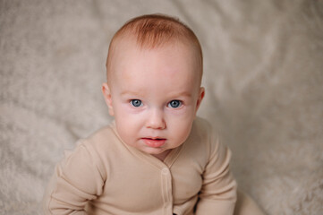 Adorable happy healthy baby boy in beige overalls sitting on bed and smiling