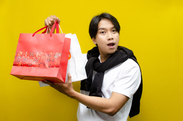 Side view of Happy Surprised Young Asian Man Holding Shopping Bags in Excitement