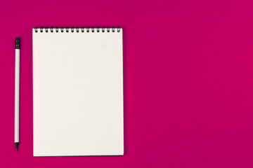 A notebook with an even spring at the top with white pages and a white pencil with a gray lead and a black eraser lie on a pink background on the left with space for text. High quality photo