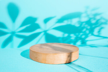 Round wooden stand on turquoise background with palm plant shadows, soft focus close up, gobo photography for product display