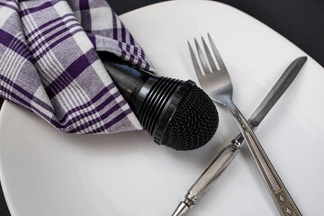 Black microphone wrapped in a purple napkin next to fork and knife on a white plate, culinary blog...