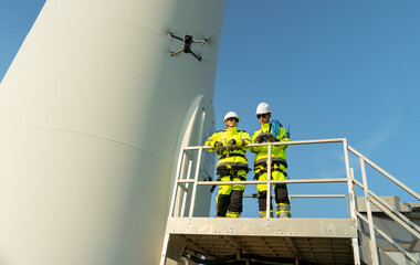 Wide shot two wind turbine or windmill workers or engineer stand on base of the pole and one...