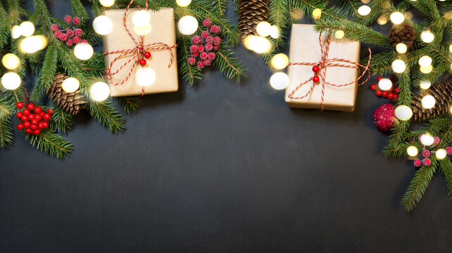 Christmas holiday background with gifts, holly berries, garland, fir tree and decoration on black background. Holiday card with copy space. Top view. Xmas card