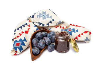 Prune jam jar or marmalade with purple plums next to an ethnic patterned fabric curtain, or tablecloth