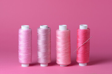 Row of many pink thread spools with needle background aligned with copy space for text close-up flat lay top view