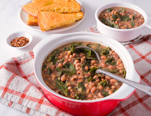 Traditional US Southern food of black-eyed peas and collard greens in a red cooking pot with corn bread