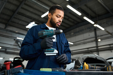 A skilled young mechanic focuses on using a power tool in a busy auto repair shop.