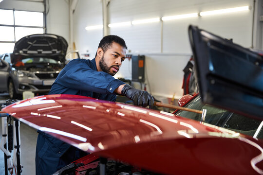 Handsome young mechanic focused on fixing a red car in a bright garage environment