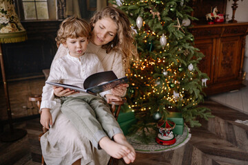 Mother reading a story to her child by a decorated Christmas tree during the holiday season