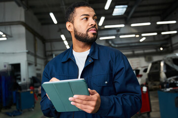 Handsome young mechanic reviews his work schedule in a modern automotive repair shop.