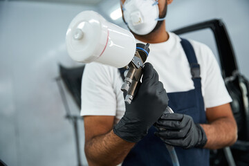 Skilled mechanic focuses intently while using a spray gun for auto body work in a garage.