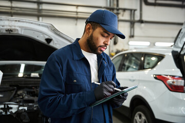 Young mechanic checks vehicle diagnostics with focus in a bustling repair shop environment.