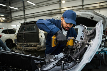 Young mechanic focuses intently while repairing car parts in a bustling auto repair shop.