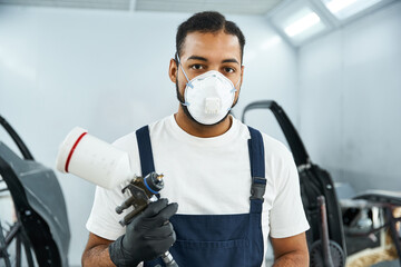 Young mechanic prepares to apply paint with an airbrush in a bright workshop environment.