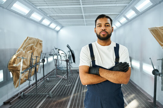 Young mechanic stands proud in a well equipped workshop, showcasing skill and readiness for work.