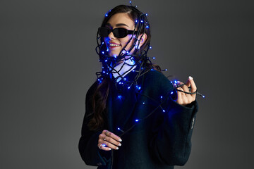 A young woman enjoys a playful moment, wrapped in bright blue string lights, smiling joyfully.